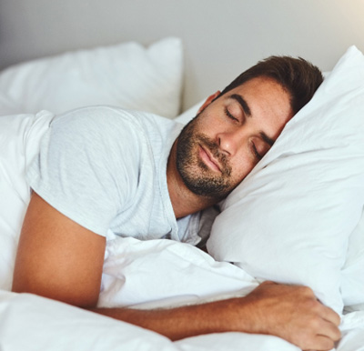 a man sleeping in a bed with white sheets