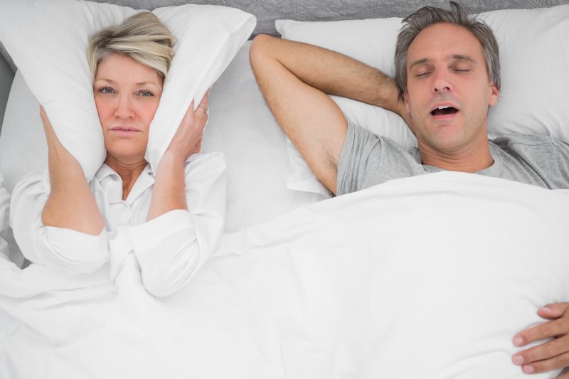 a woman with a pillow over her ears while her husband snores