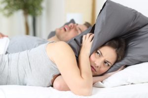 woman using pillow to block sound of husband's snoring