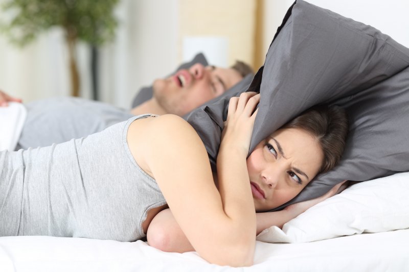 woman covering ears with pillow while partner snores