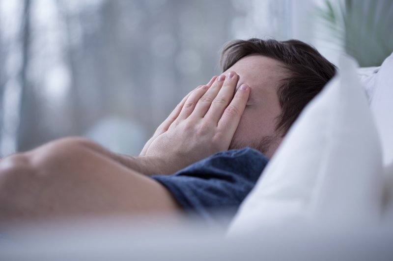 Man lying in bed awake and covering his face