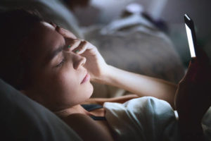 Woman laying in bed looking at her cell phone
