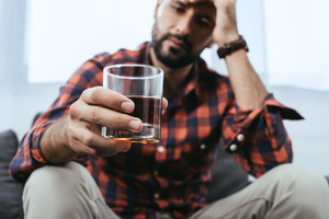 Man in chair holding and staring at alcoholic beverage