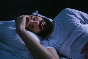 Bearded man with sleep apnea lying awake in bed