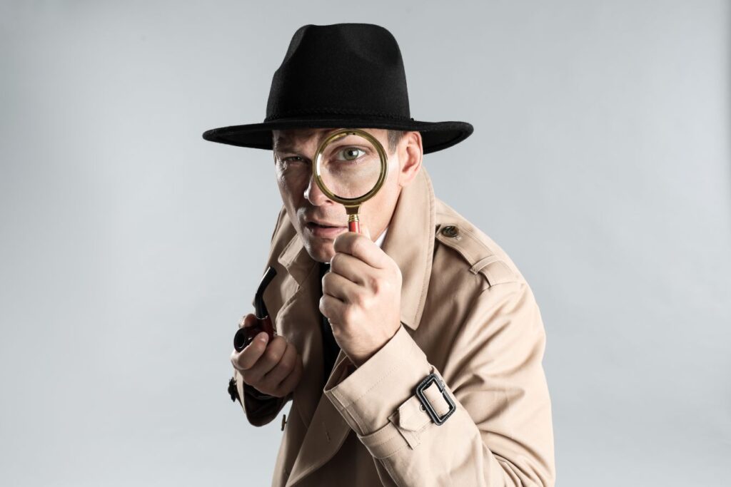 A man dressed as a detective looking through a magnifying glass.