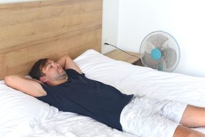 Man lying in bed, sleeping next to a fan